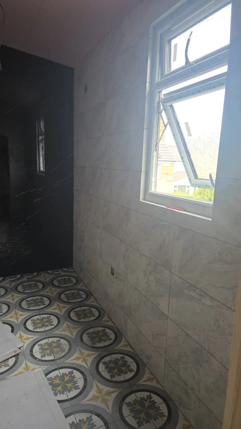 Marble-effect wall tiles beside a window and a patterned tiled floor