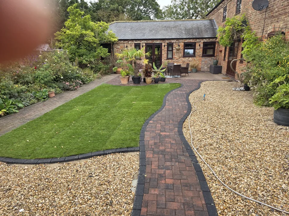 A brick path, gravel border and lawn in a cottage courtyard