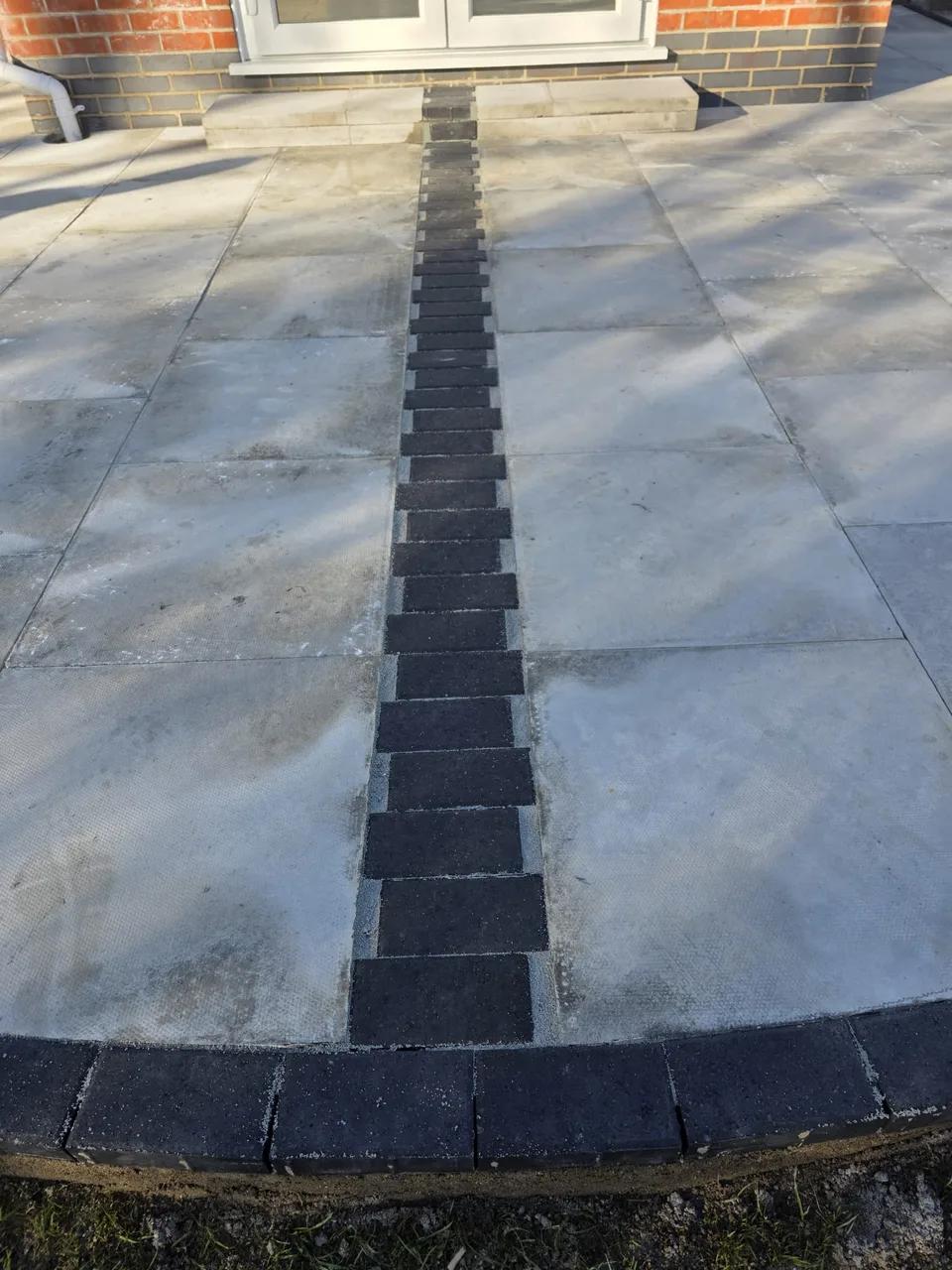 Dark brick edging and a central pattern between stone patio slabs