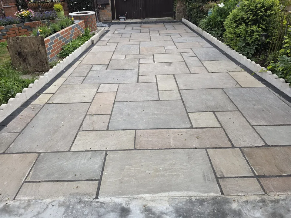 Rectangular stone paving bordered by dark edging and flower beds