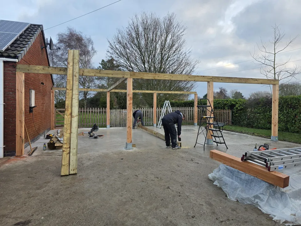 Timber posts and beams being assembled beside a brick building